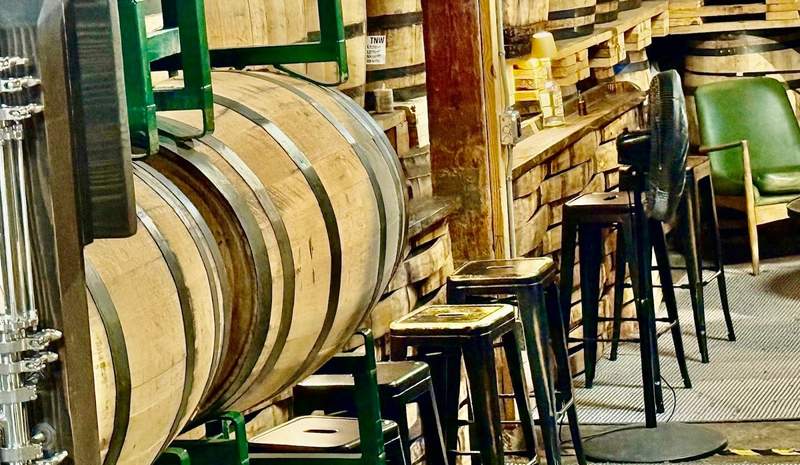 Long-legged stools, some with low backs, sit in front of big wooden barrels to form a tasting room for whiskey.