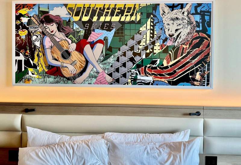 One large horizontal painting over the hotel bed shows a girl dozing with her guitar. Four bed pillows look fluffy and inviting.