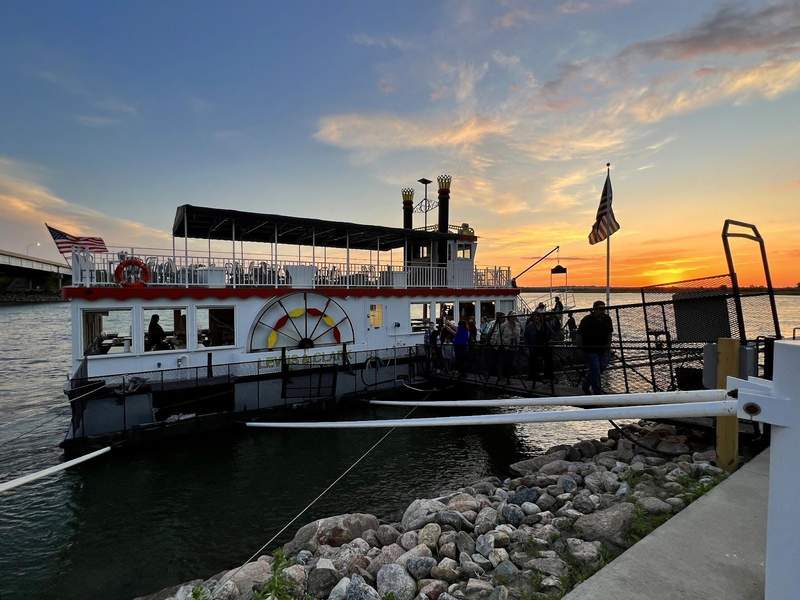 A white paddleboat with a canopied upper level on the water at sunset
