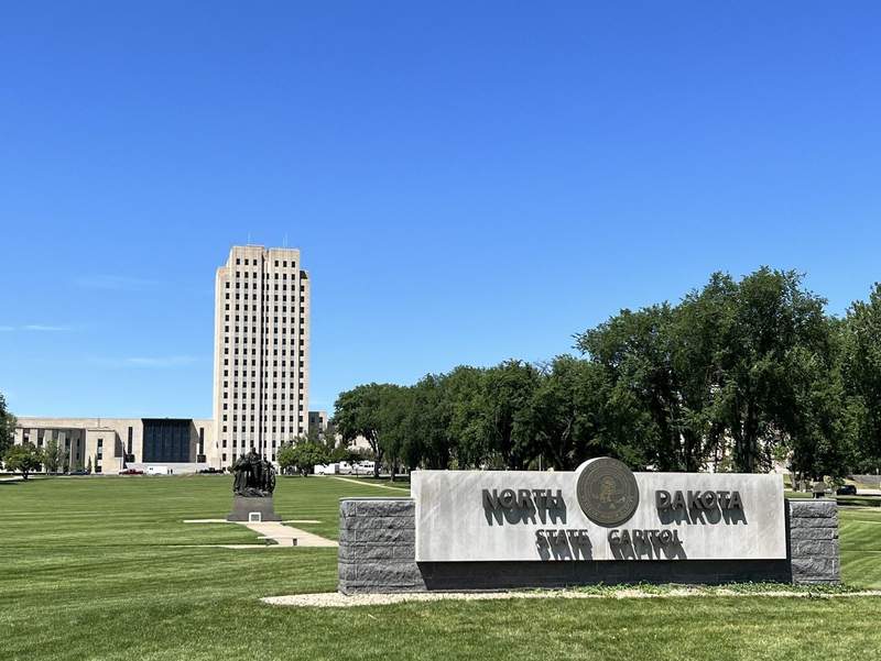 A tree lined grassy mall with sign that reads North Dakota State Capitol. the 21 story skyscraper is in the background