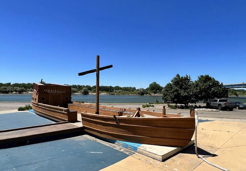 A shallow wooden boat with an enclosed sleeping and storage compartment at one end and an empty mast at the center.