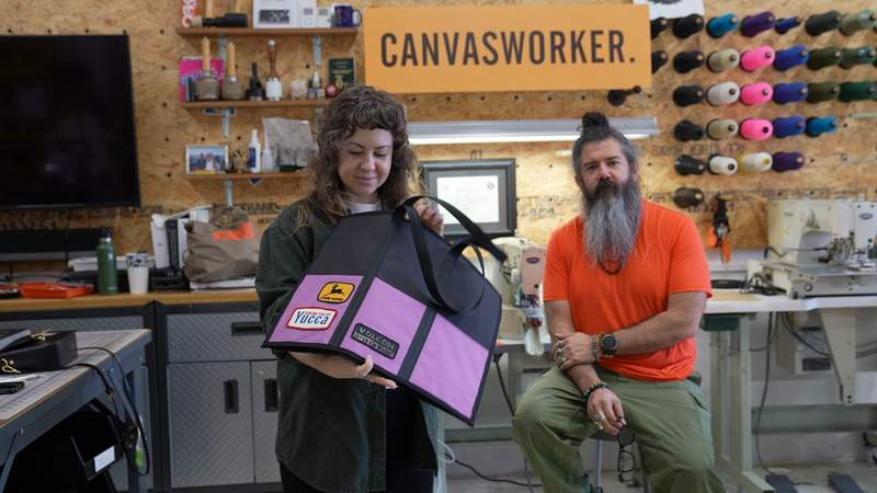 A woman holds a custom self-designed tote from Canvasworker while a bearded man looks on from behind.