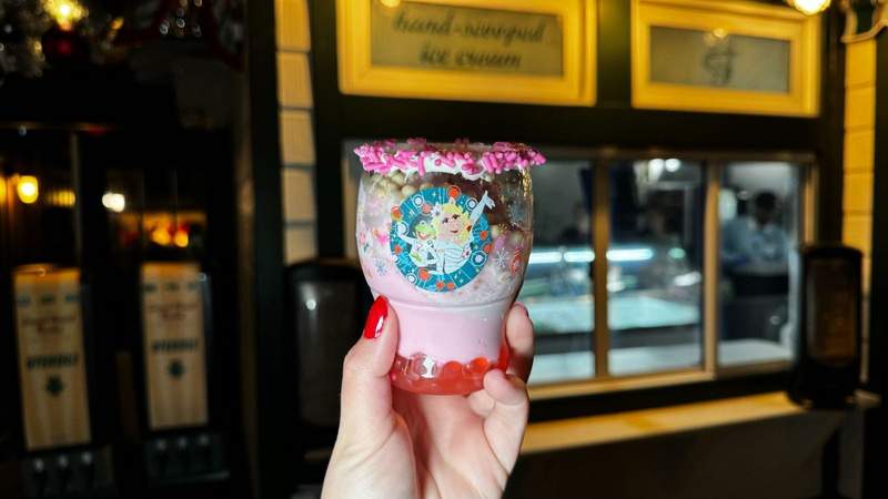 Hand holding a plastic cup decorated with Miss Piggy and Kermit filled with strawberry pink ice cream. 