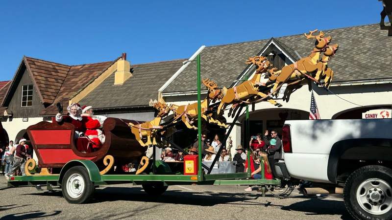 white truck and wooden reindeer pushing a sleigh float with two individuals santa and mrs claus at solvang julefest