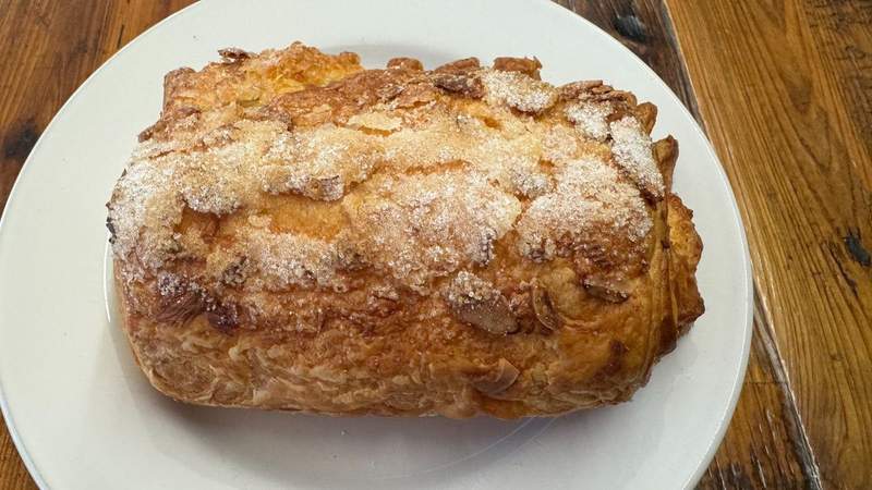 Pastry with almond slices and sugar on a white plate on a wooden table in Solvang