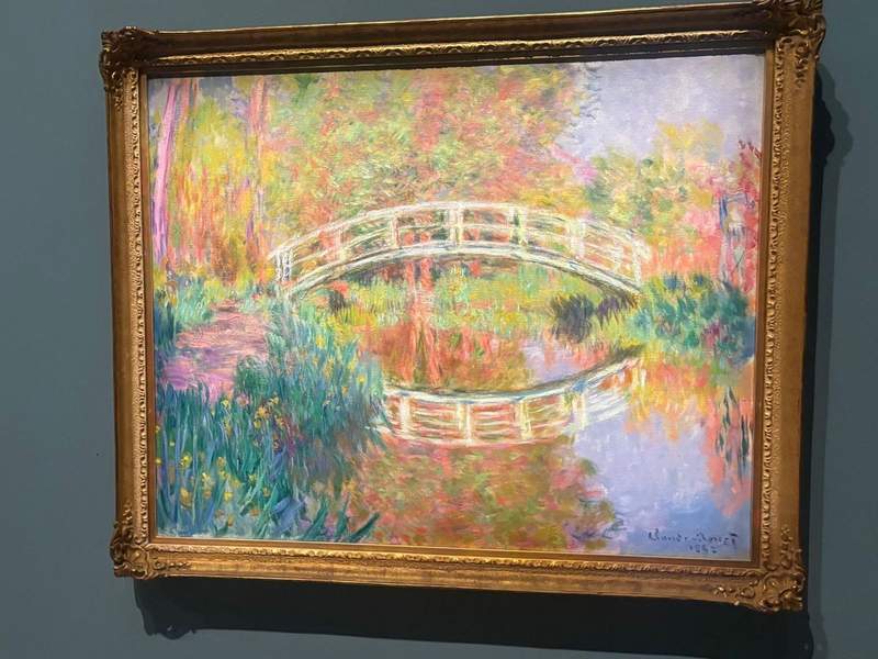 Colorful Monet painting with trees and a bridge.