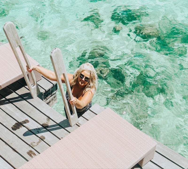 woman climbing a ladder from the ocean into an overwater bungalow in Tahiti during a PTO-stacked vacation