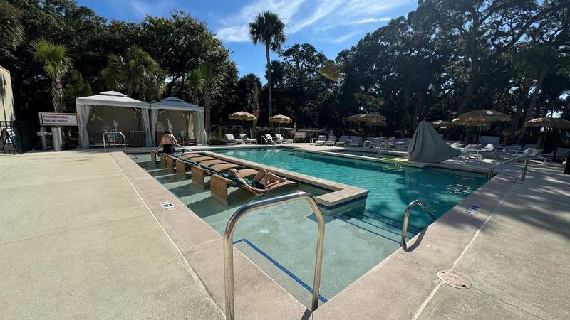 pool with beige lounge chairs and two white cabanas on pavement at Sonesta Resort Hilton Head Island. 