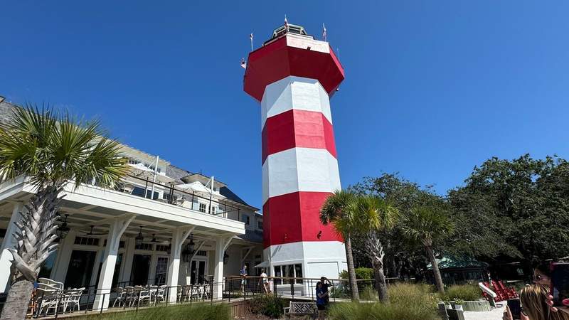 red and white striped lighthouse next to palm trees and a white building at Coligny beach