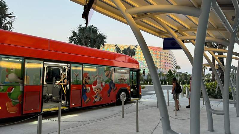 A red bus decorated with Mario characters in front of a hotel bus stop. 