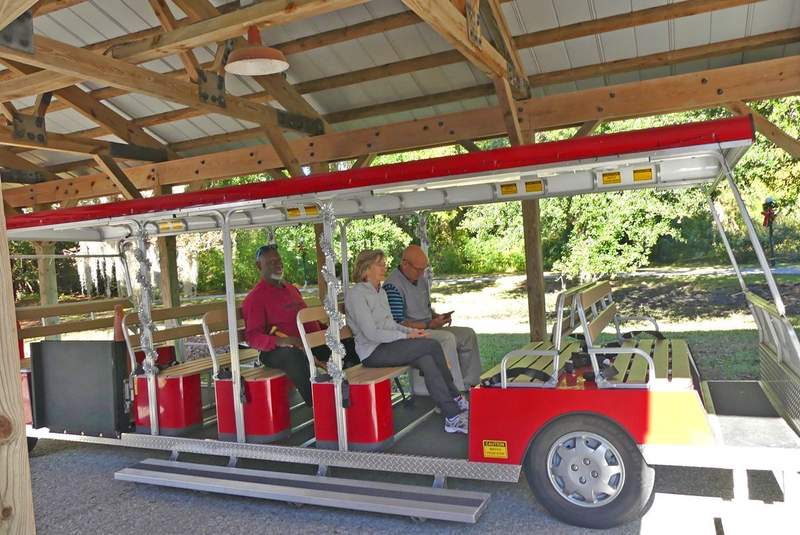 A bright red trolley car with three passengers aboard.
