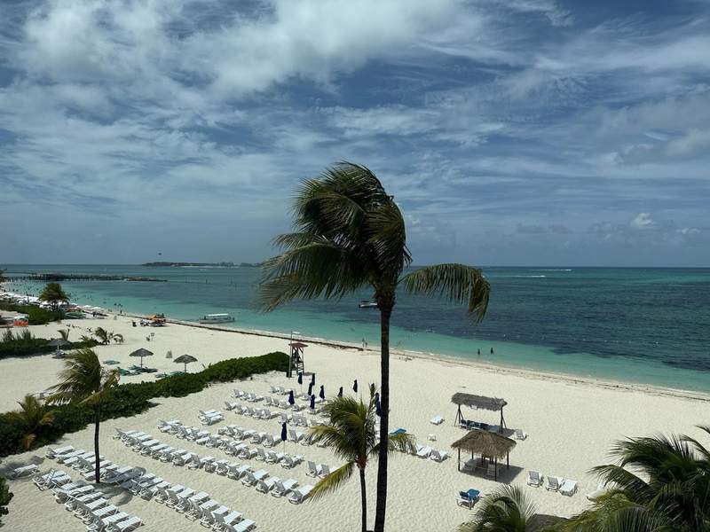 Photo shows the view from room overlooking the beachfront at Breezes Bahamas. It shows lounge chairs on the beach palm trees blowing in the breeze and a view of the beachfront