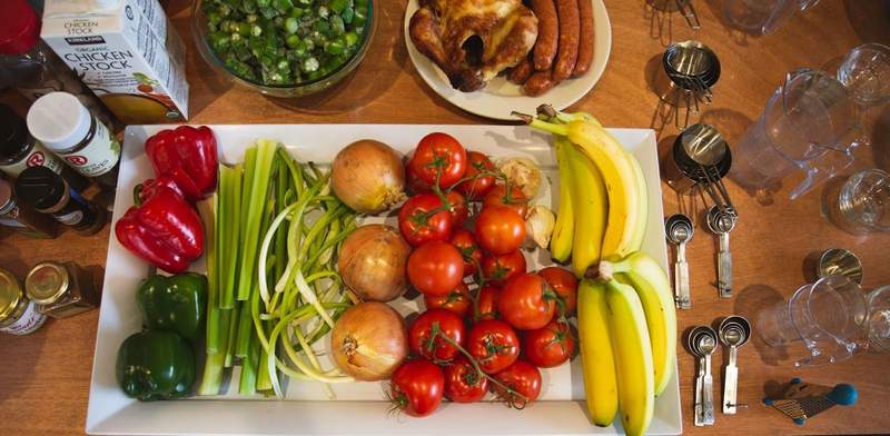 Ingredients for Creole Recipes displayed on a cutting board that include peppers celery onions okra tomatoes and other meats vegetables and spices.