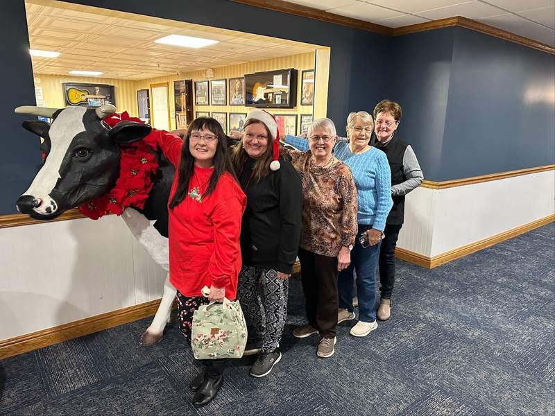 Five ladies standing in front of a cow statue.