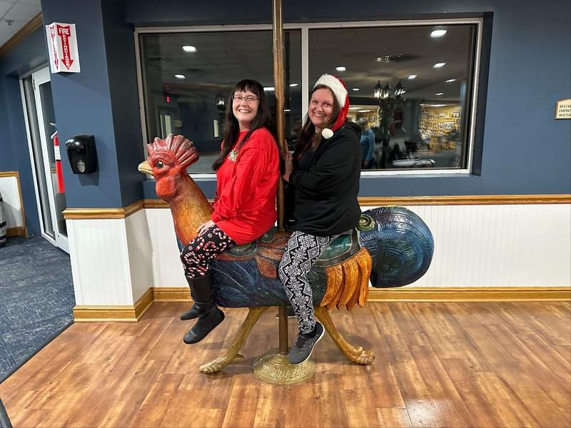 Two women sitting on a chicken statue.