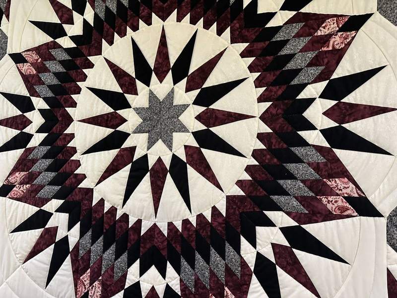 A cream maroon grey pink and black quilt with a star pattern. 