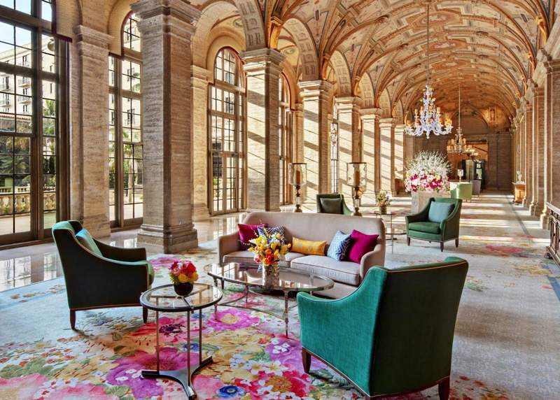Green chairs colorful couch and high tan arched ceiling in lobby of The Breakers resort in Palm Beach Florida