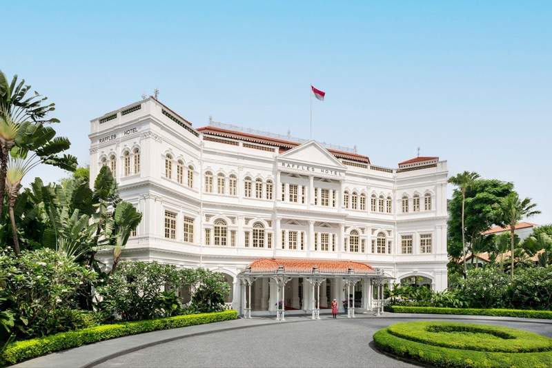 White facade of Raffles Hotel Singapore with greenery surrounding