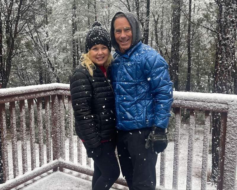 Couple outdoors at a ski mountain in light snowfall showcasing two different travel styles.