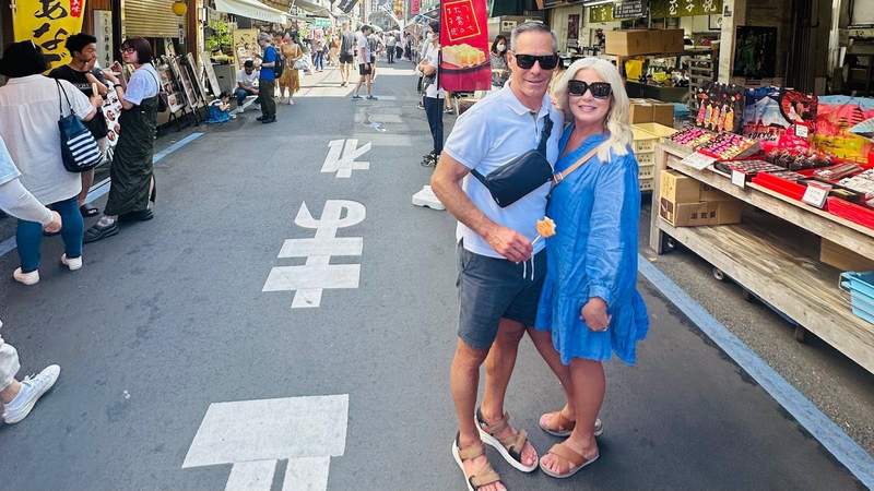 Couple standing together at Tsukiji Fish Market in Tokyo surrounded by food stalls.