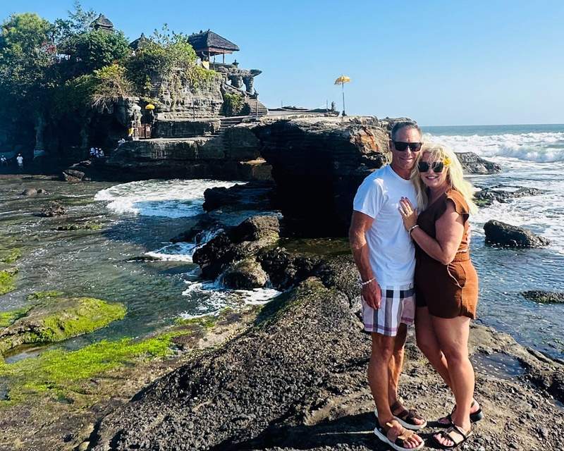 Couple visiting Tanah Lot in Bali with ocean scenery and a rocky shoreline surrounding them.