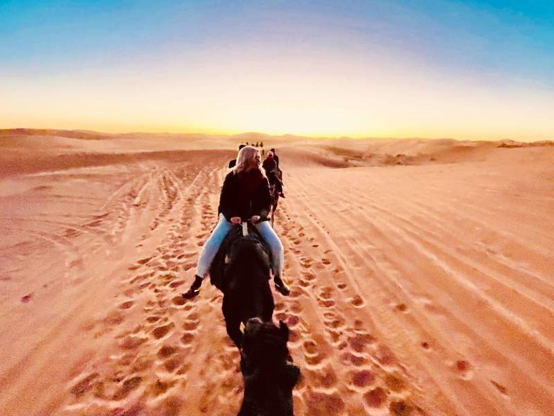 A woman riding a camel in the Sahara Desert at sunrise. 