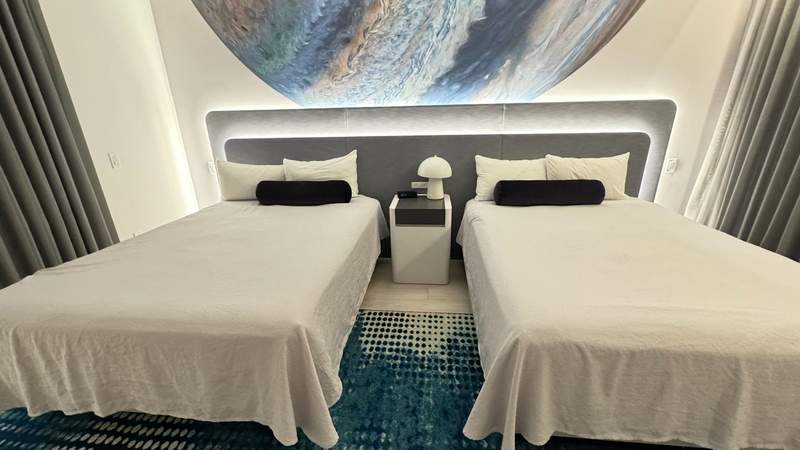 two queen beds in a bedroom with pillows infront of a planet painting on a blue and yellow carpet at Universal Terra Luna Resort Orlando. 