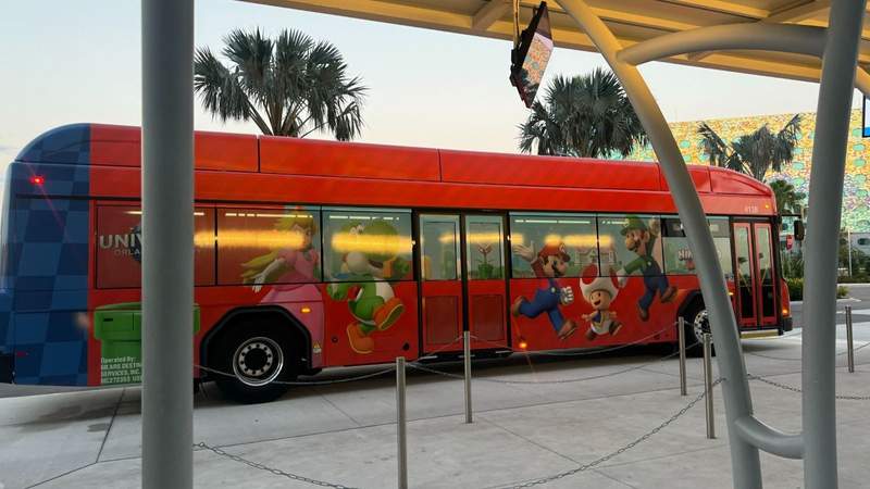 red bus with mario kart characters in front of palm trees and a queue outside of Universal Terra Luna Resort Orlando. 