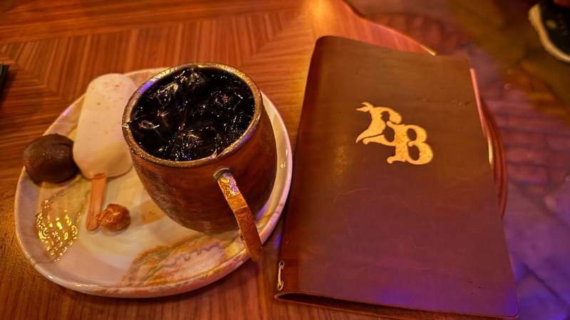 leather menu with gold BB letters on the front next to a plate with a gold mug white cake pop and chocolate ball at The Beak and Barrel. 