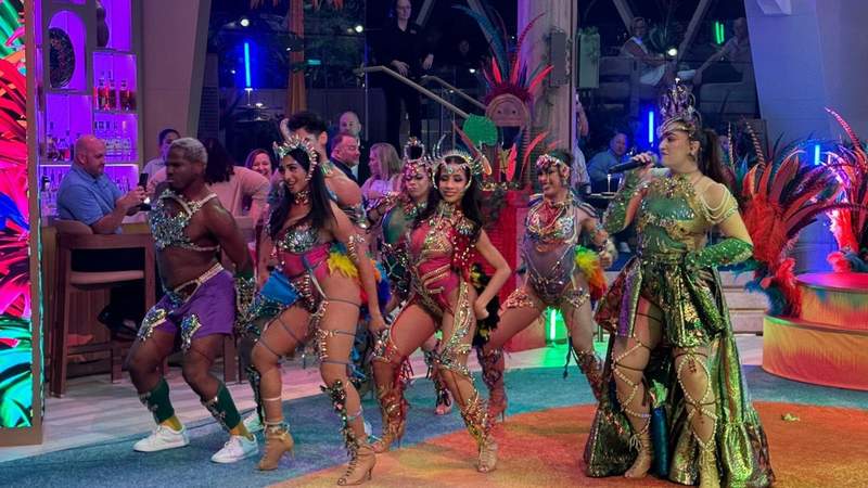 six dancers and a singer in shiny theatrical outfits performing on the celebrity xcel