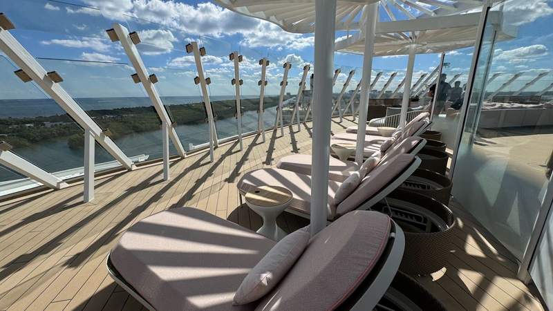 lounge reclining chairs on a wooden deck behind glass panels looking into the ocean on the celebrity xcel