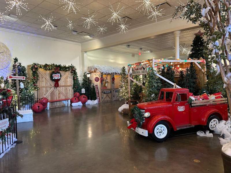 A room filled with Christmas Decorations including a red truck pine trees snowflakes hanging from the ceiling and other photo opportunities in the Visitor Center.