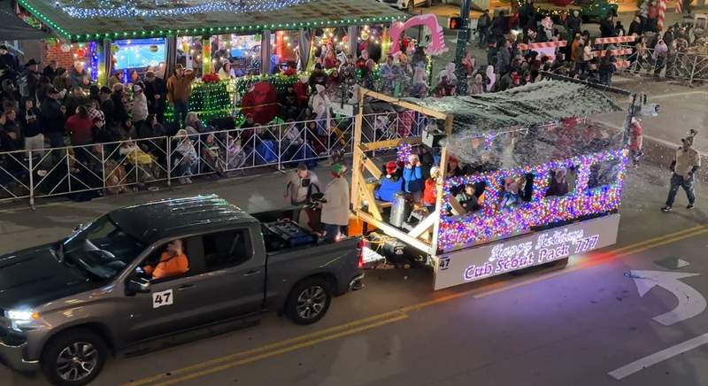 A colorful float in a parade pulled by a grey truck.