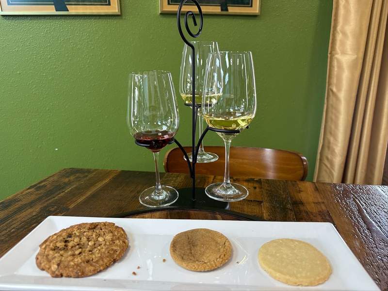 Three glasses with wine in them and three different cookies on a plate.