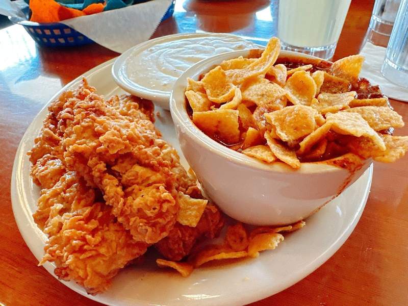 A bowl of chili with corn chips on top and some chicken fried steak on a plate.