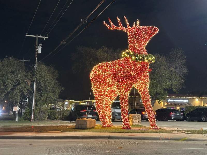 A large reindeer statue covered in red lights with a wreath around the neck.