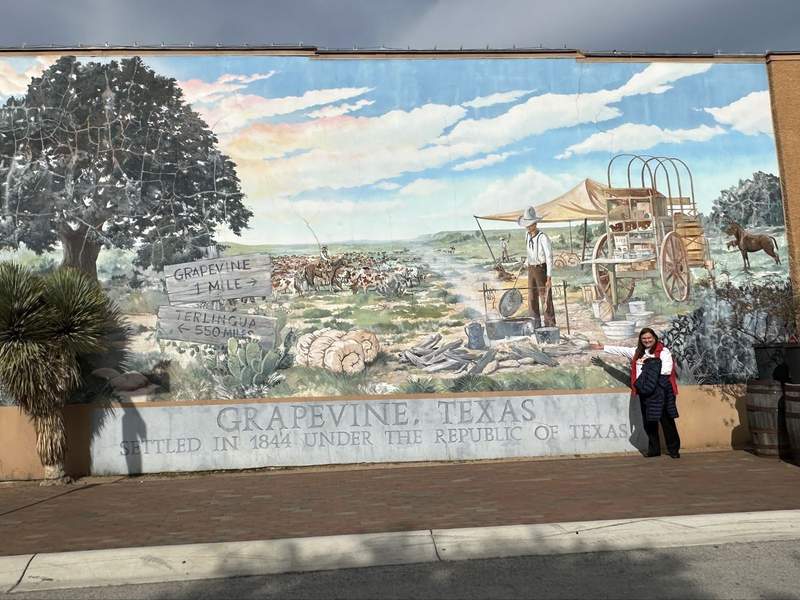 A woman in front of the Grapevine Texas mural.