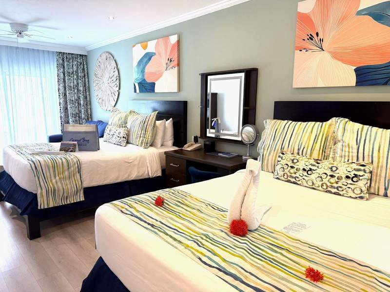 Caribbean Bay Harmony room decorated with white blue and green linens. Two queen beds with desk between and floral pictures above.