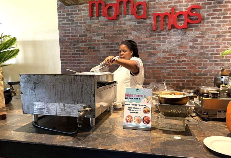 Cook to order station with sign reading Mama Mias with a woman holding tongs over a stove.