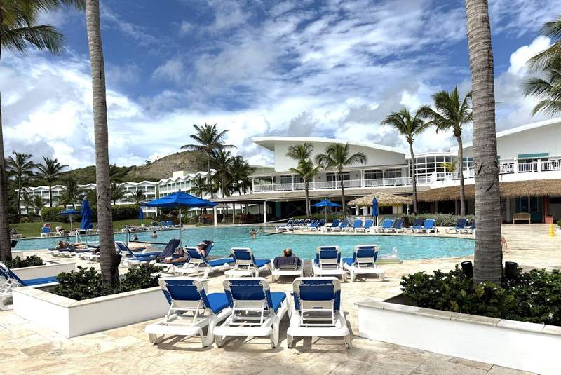 Pool area with chaises in front of a two story building and palm trees.