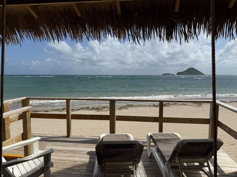 View from cabana with thatched roof and railing with chaise lounges of beach and the Maria islands.