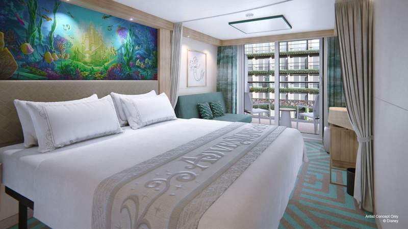 A spacious stateroom aboard Disney Adventure features undersea themed artwork a queen sized bed couch and a view of the ships lush interior courtyard.