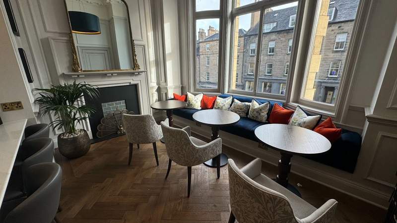 bright windows and three chairs and a navy blue booth with accent pillows and hardwood floors in a lounge at righ residences edinburgh