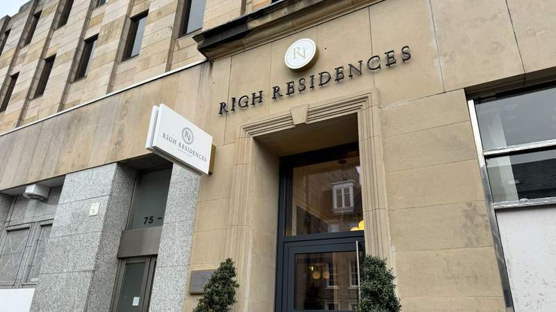 building with righ residences logo and two trees a small white placard with the hotel logo