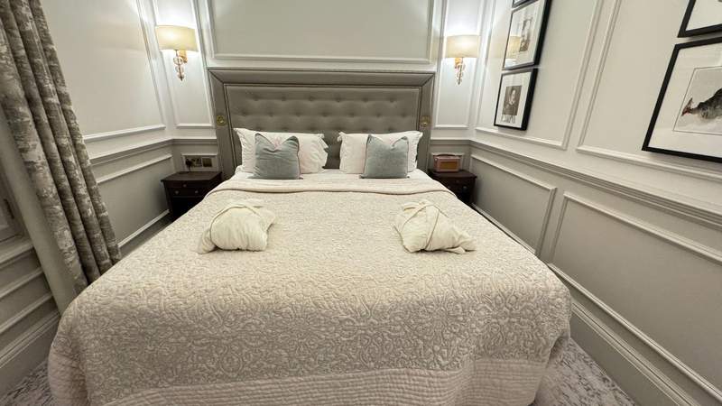 king bed in a room with robes folded on top and throw pillows with paintings on the wall next to grey curtains at righ residences edinburgh