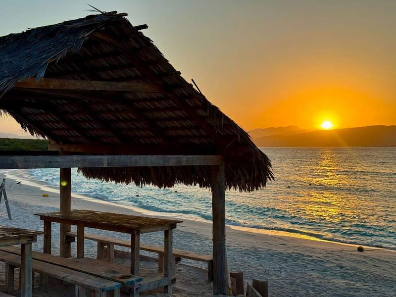 A palapa in the sand by the sea with mountains in the background