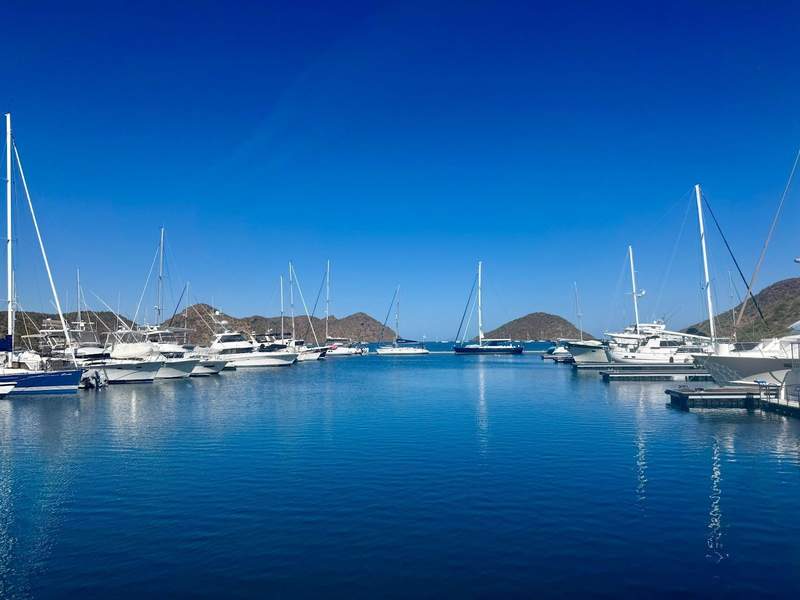 Yachts in a marina of still blue water with mountains in the background