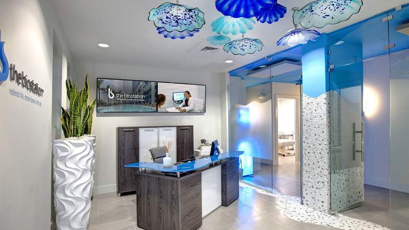 A doctors office waiting room. A small desk in is the middle and blown glass flowers in blue and green hang from the ceiling.
