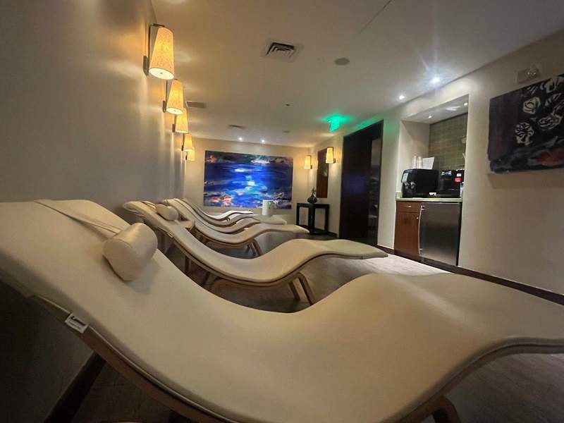 Cream colored reclining spa chairs line a dimly lit comfortable waiting area inside a spa.