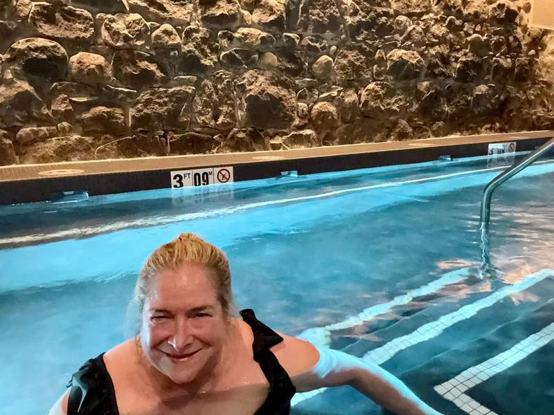 Woman in the large hot tub with  a stone wall and dim lighting.